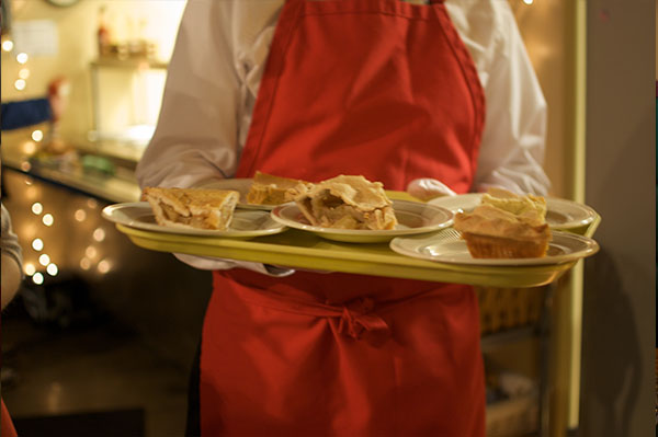 a person with a red apron holds a tray of pie pieces. Featured shoulders down.