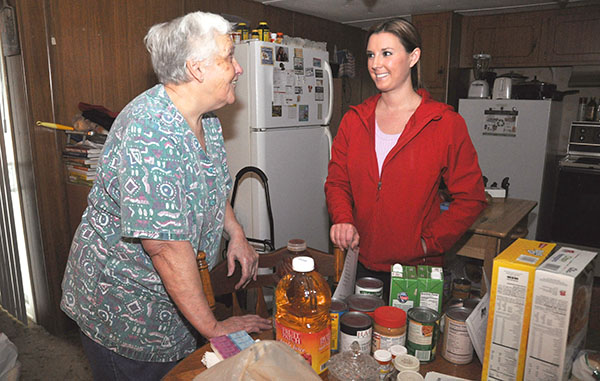 an older woman speaks with a younger woman across a table of food donations