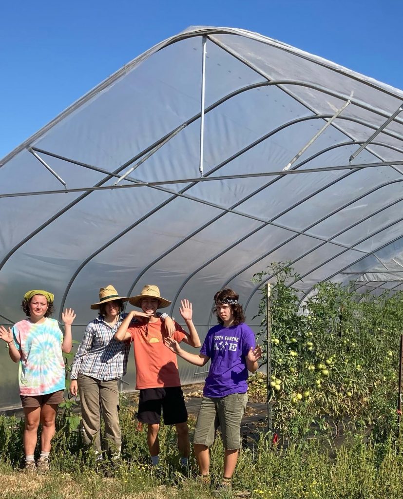 four youth farmers in summer attire pose beneath the new grow tunnel at the youth farm